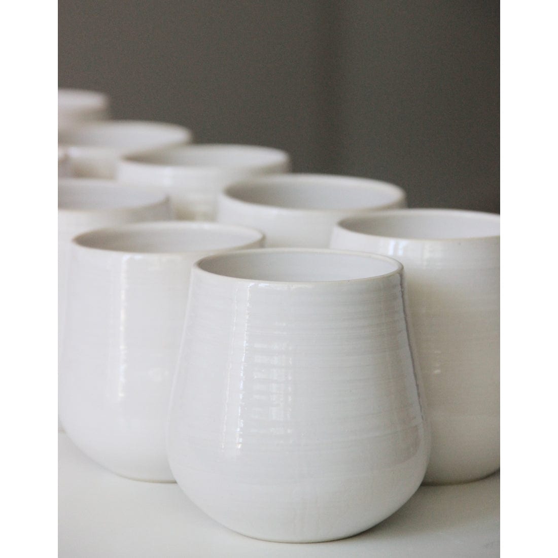 white handmade ceramic tumblers lined up on an exposed shelf