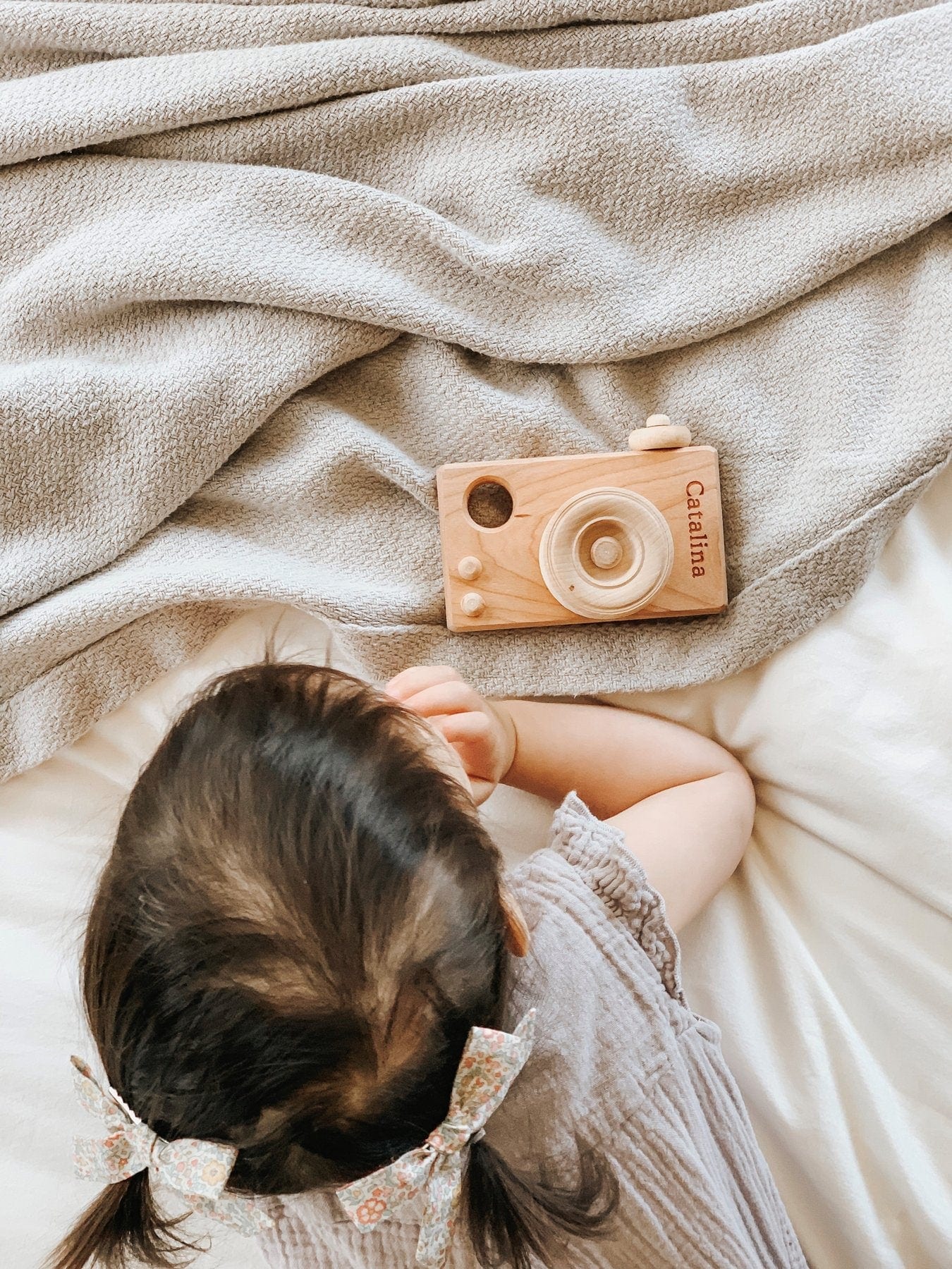 girl playing with wooden toy camera on a bed