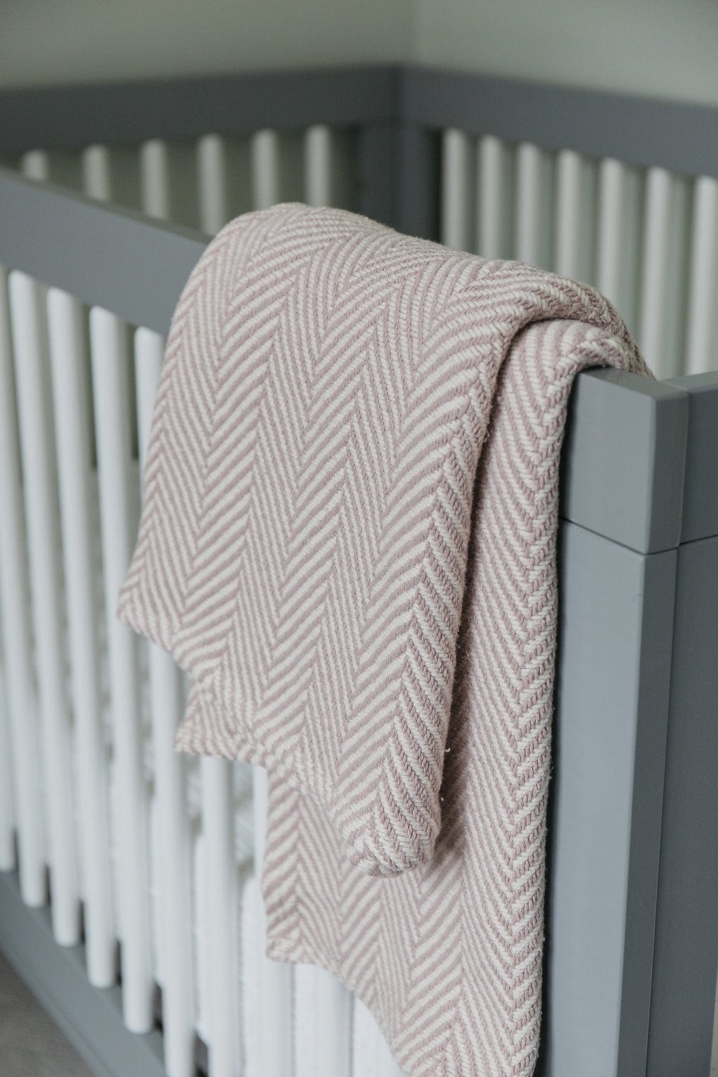 herringbone baby blanket finished in blush color draped over a crip