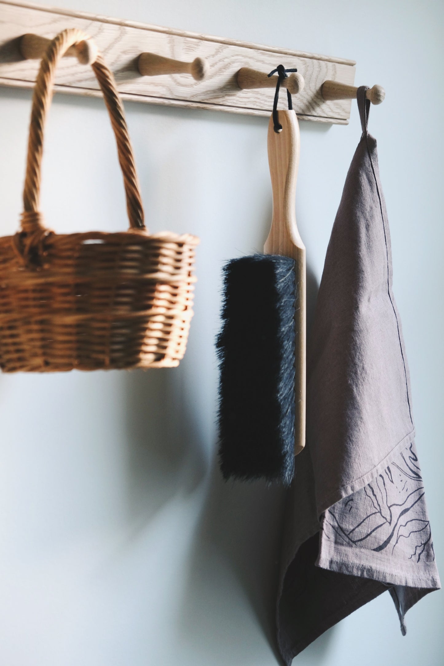 Brush, basket, and tea towel hanging on a peg rail. 