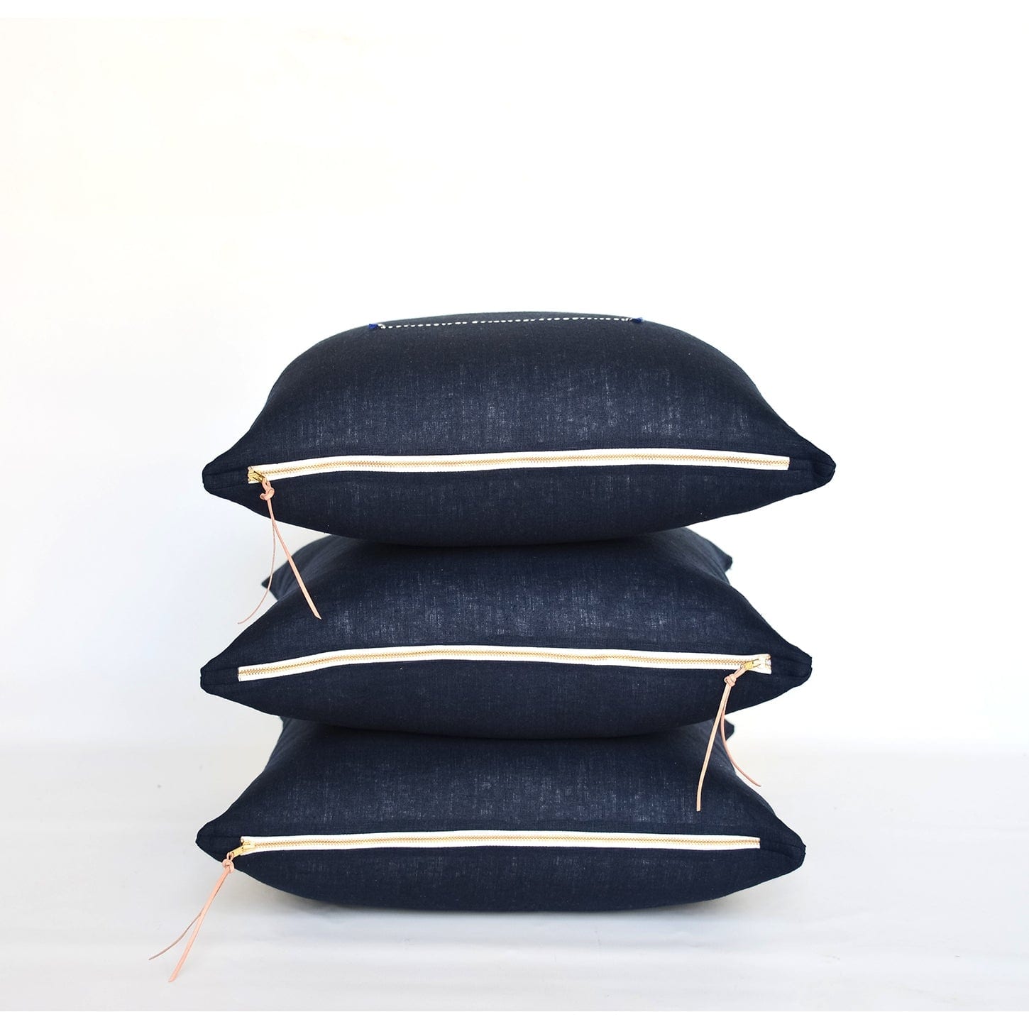 3 stacked Navy Linen Pillows with brass zipper and leather tassels