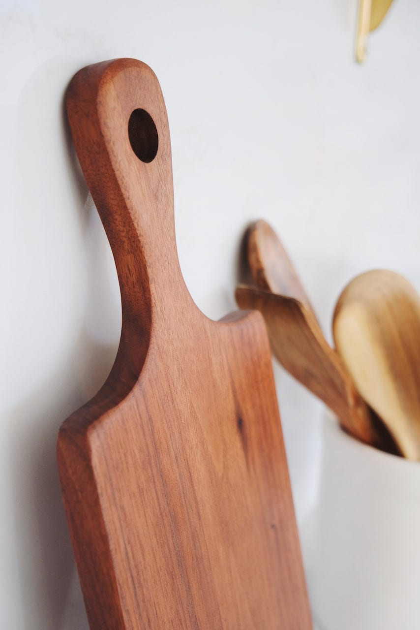 cherry handled hardwood serving board leaned up against a backsplash