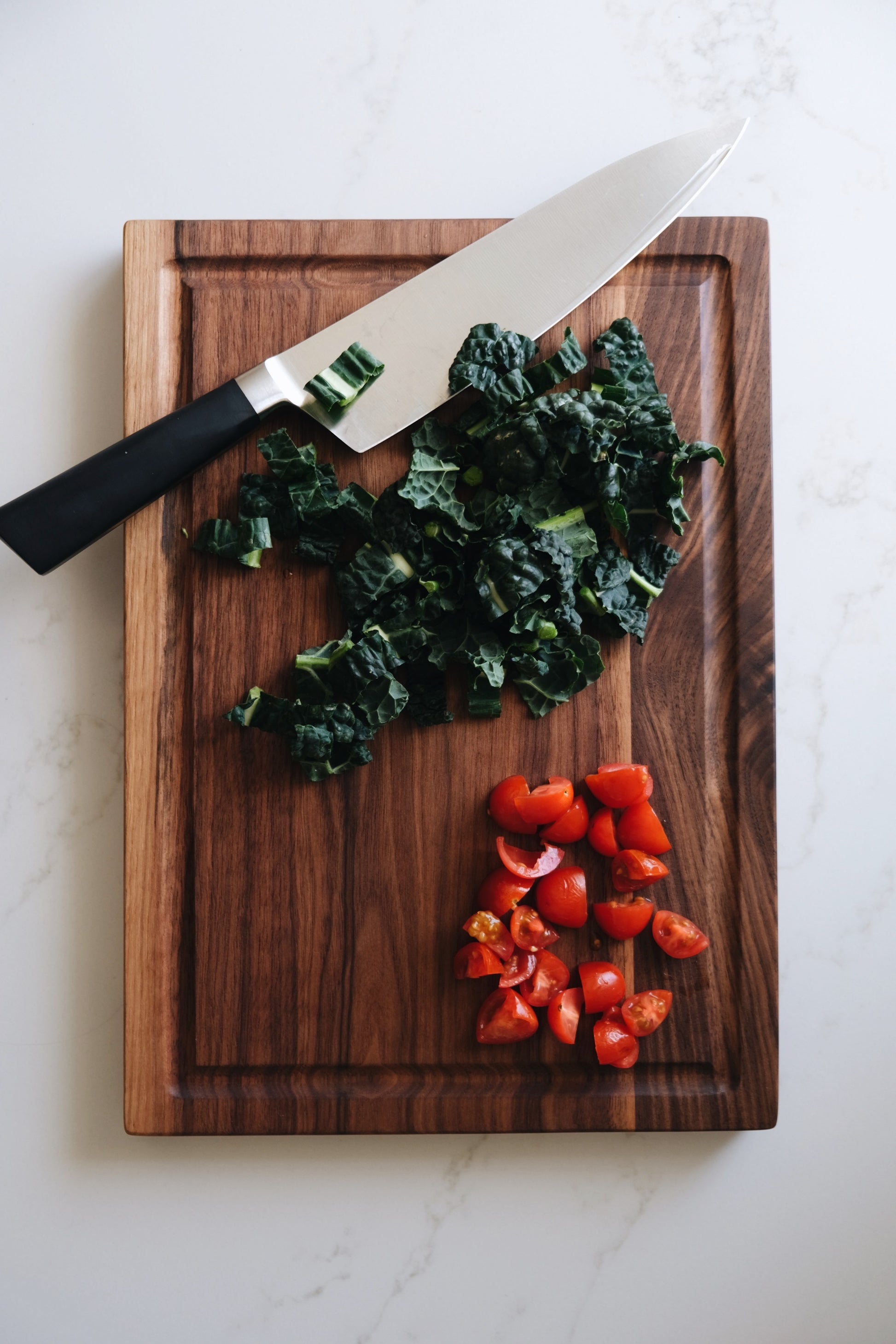 walnut cutting board with tomatoes and kale on top. 
