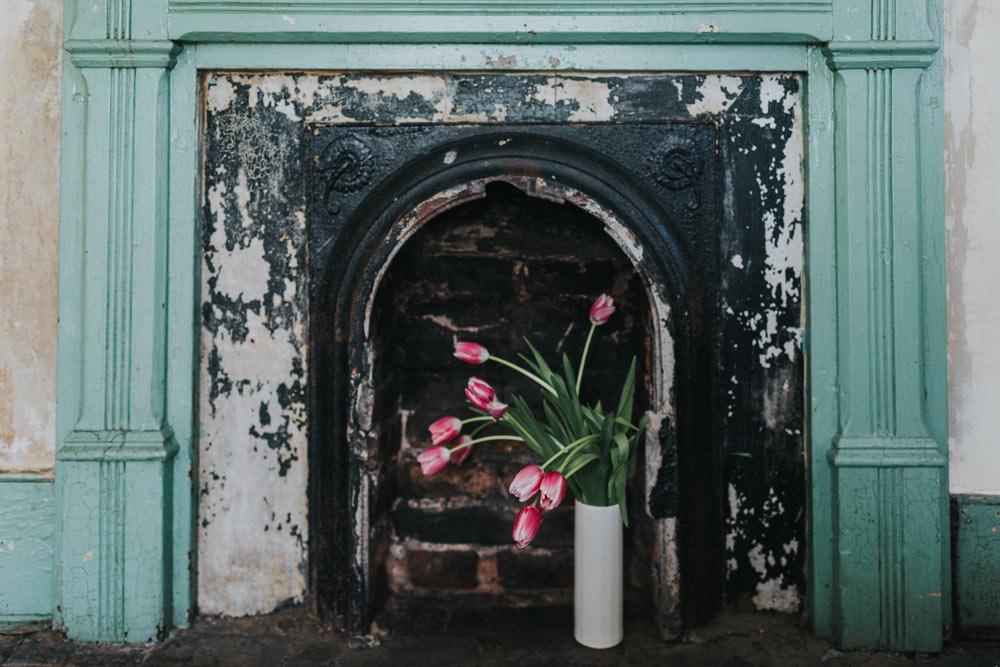 flower vase holding tulips beside a fireplace