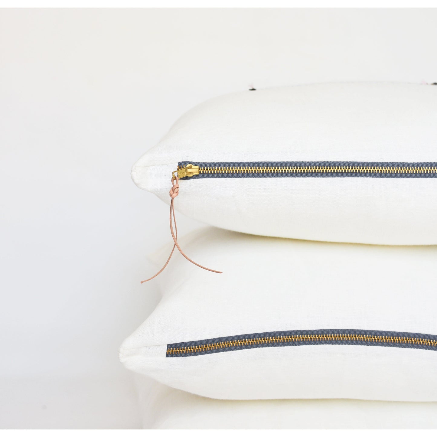 White lumbar linen pillow with brass zipper and leather tassel
