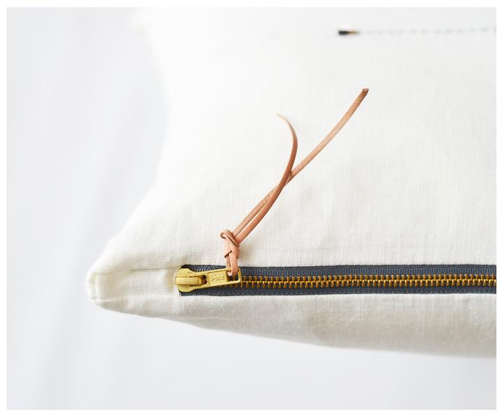 Close up of leather tassel and brass zipper on white linen pillow. 
