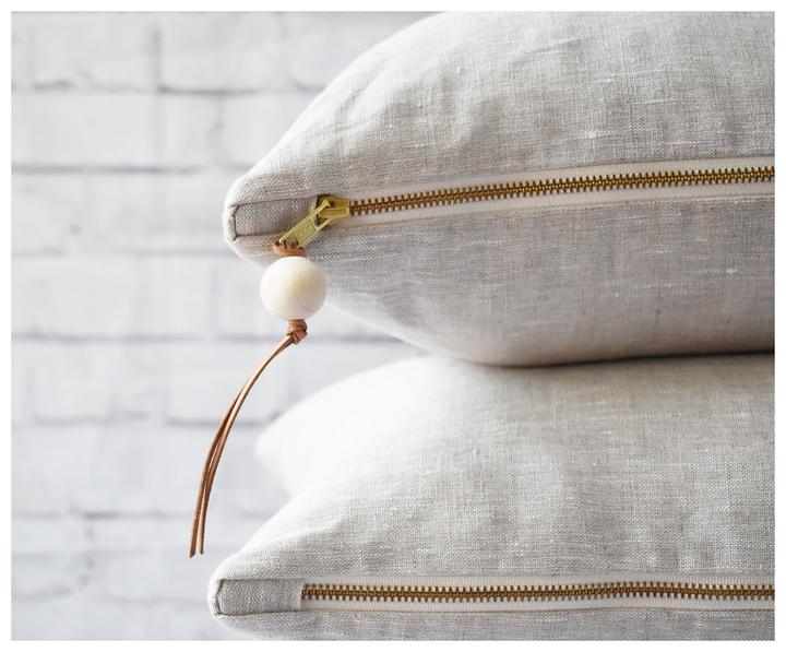 Leather Tassel attached to a brass zipper on an oatmeal lumbar linen pillow