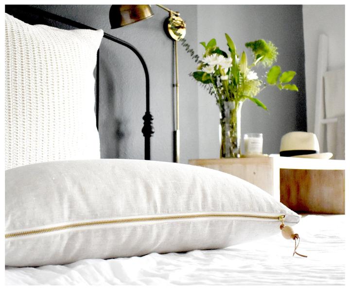 Oatmeal Lumbar Linen Pillow lying down on top of a bed with brass zipper exposed